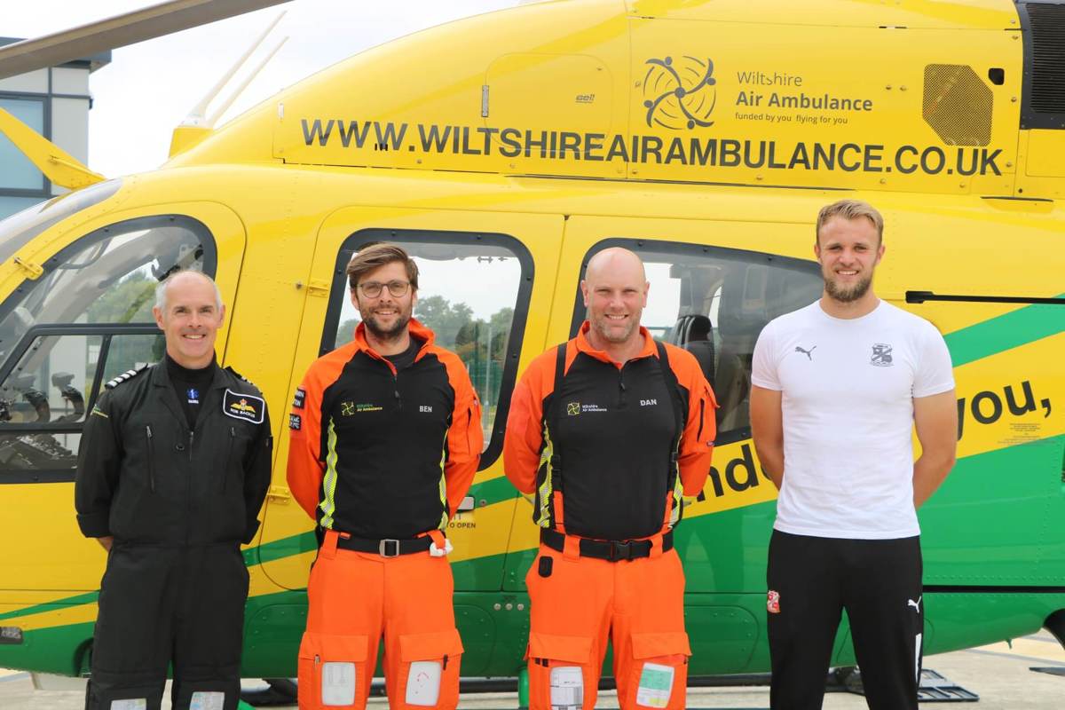 Wiltshire Air Ambulance paramedics and pilot with Swindon Town goalie Lewis in front of Wiltshire Air Ambulance's yellow and green helicopter