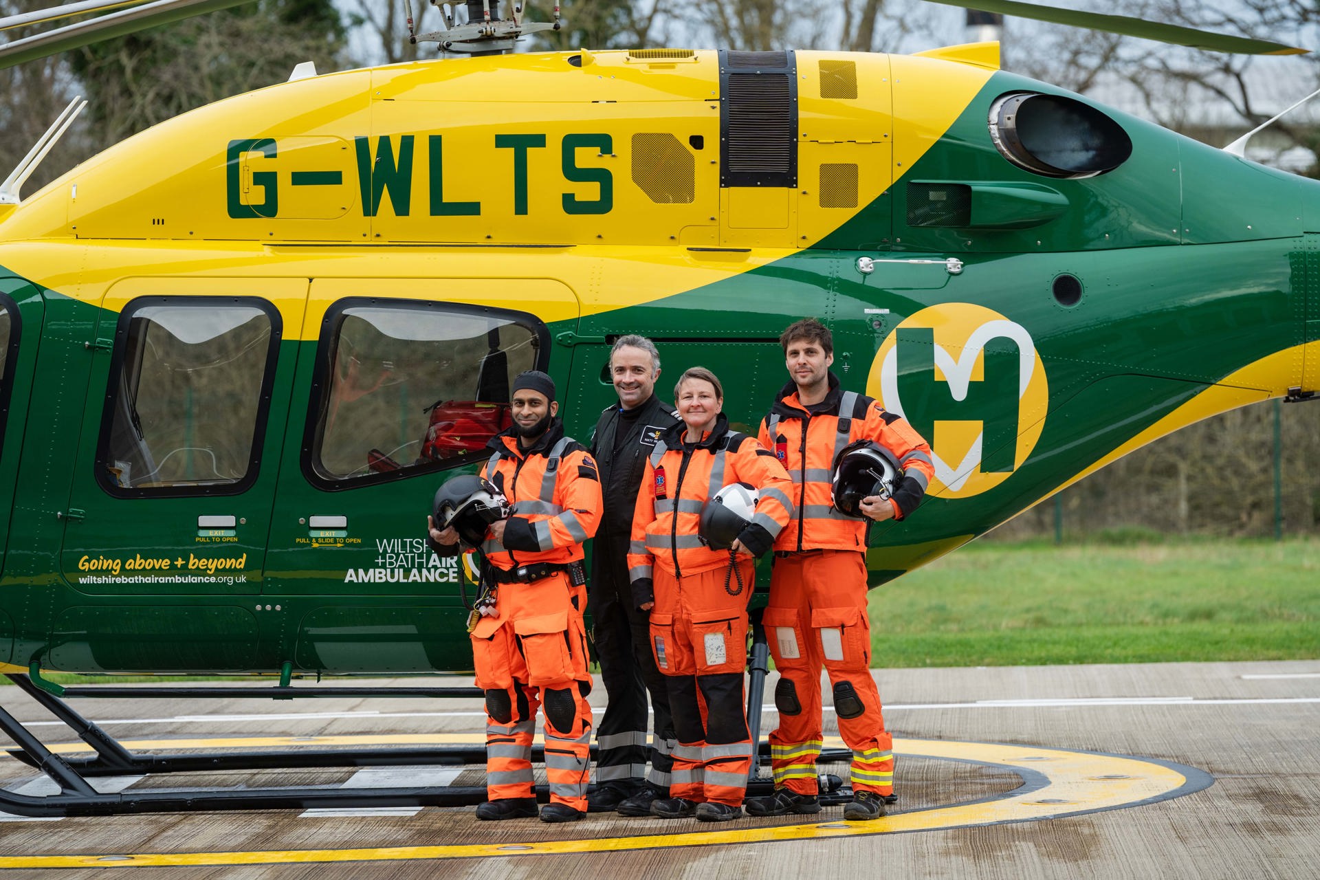 A group of air ambulance colleagues standing in front of a yellow and green helicopter A group of air ambulance colleagues standing in front of a yellow and green helicopter