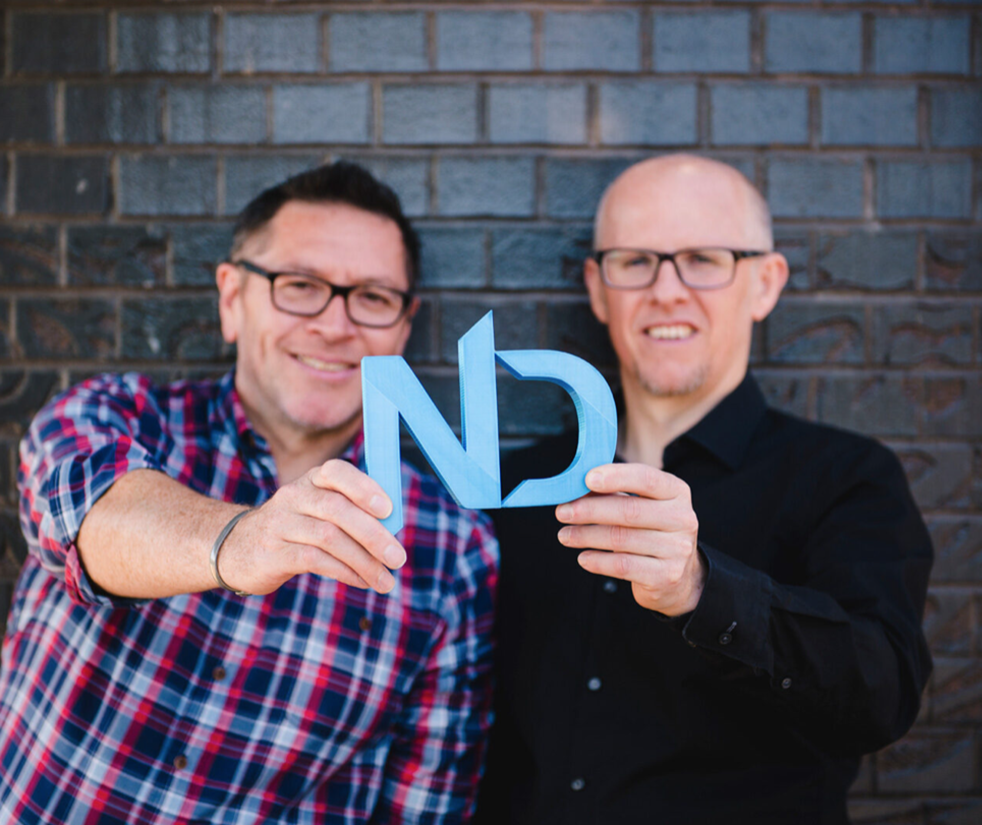 Two people holding a sign which is blue and has the letters N and D