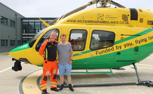 A former patient meeting critical care paramedic at the charity's airbase. They are stood in front of the helicopter on the helipad.
