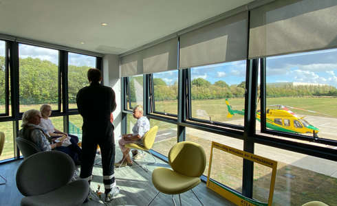 Pilot talking to 3 supporters in a room overlooking the Wiltshire Air Ambulance helicopter and helipad