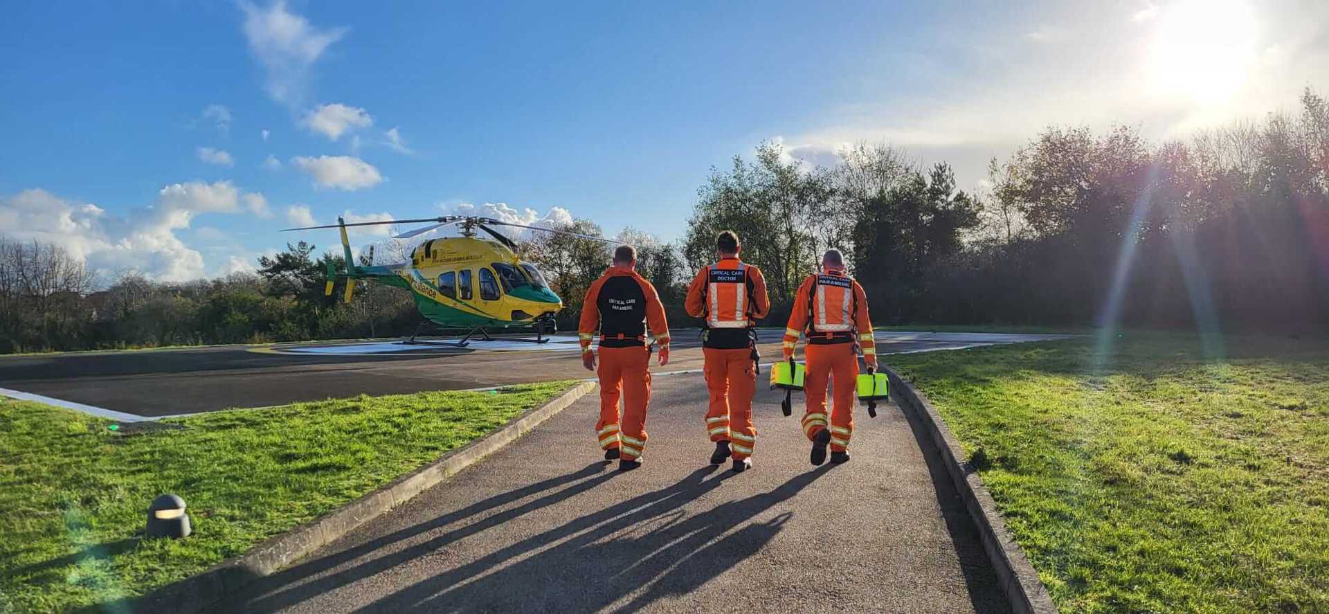Three paramedics walking towards the helicopter which has landed on a hospital helipad.