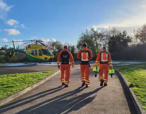 Three paramedics walking towards the helicopter which has landed on a hospital helipad.