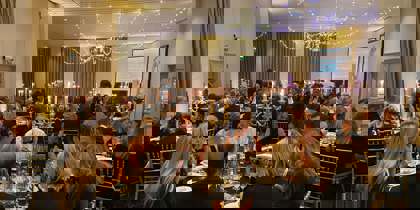 Black and gold themed charity ball. Groups of people wearing smart clothing, sitting on gold chairs around round tables