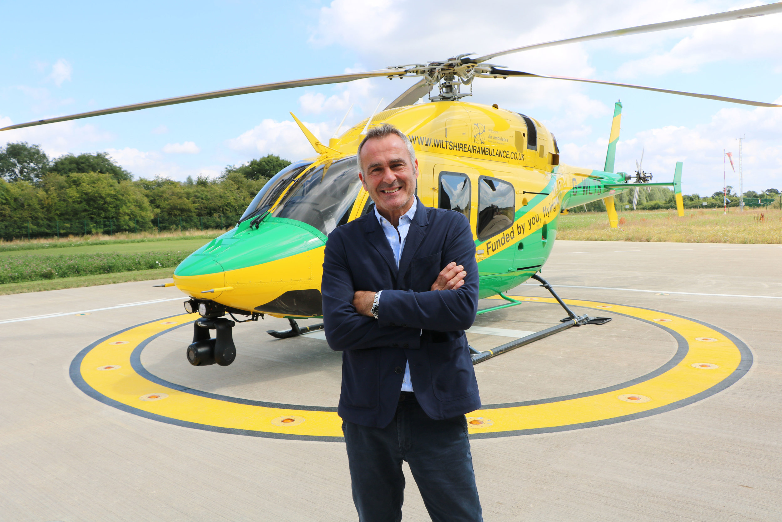 Paul Martin standing in front of a yellow and green helicopter with his arms folded