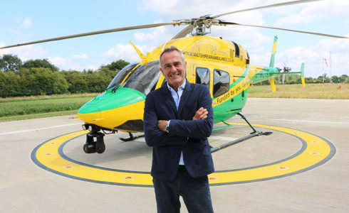 Paul Martin standing in front of a yellow and green helicopter with his arms folded