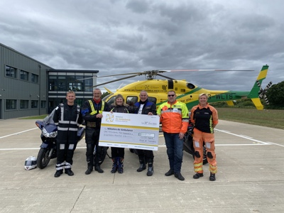 A cheque presentation with the NHS Ride of Thanks bikers with Pilot Fin Collins and Paramedic Emma Thompson in front of the Wiltshire Air Ambulance helicopter