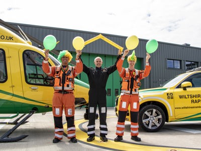Paramedic Rich Miller wearing a yellow and green curly wig and holding yellow and green balloons, Rob Backus holding yellow Team WAA cheer sticks and Craig Wilkins wearing a yellow and green mohawk wig and holding yellow and green balloons