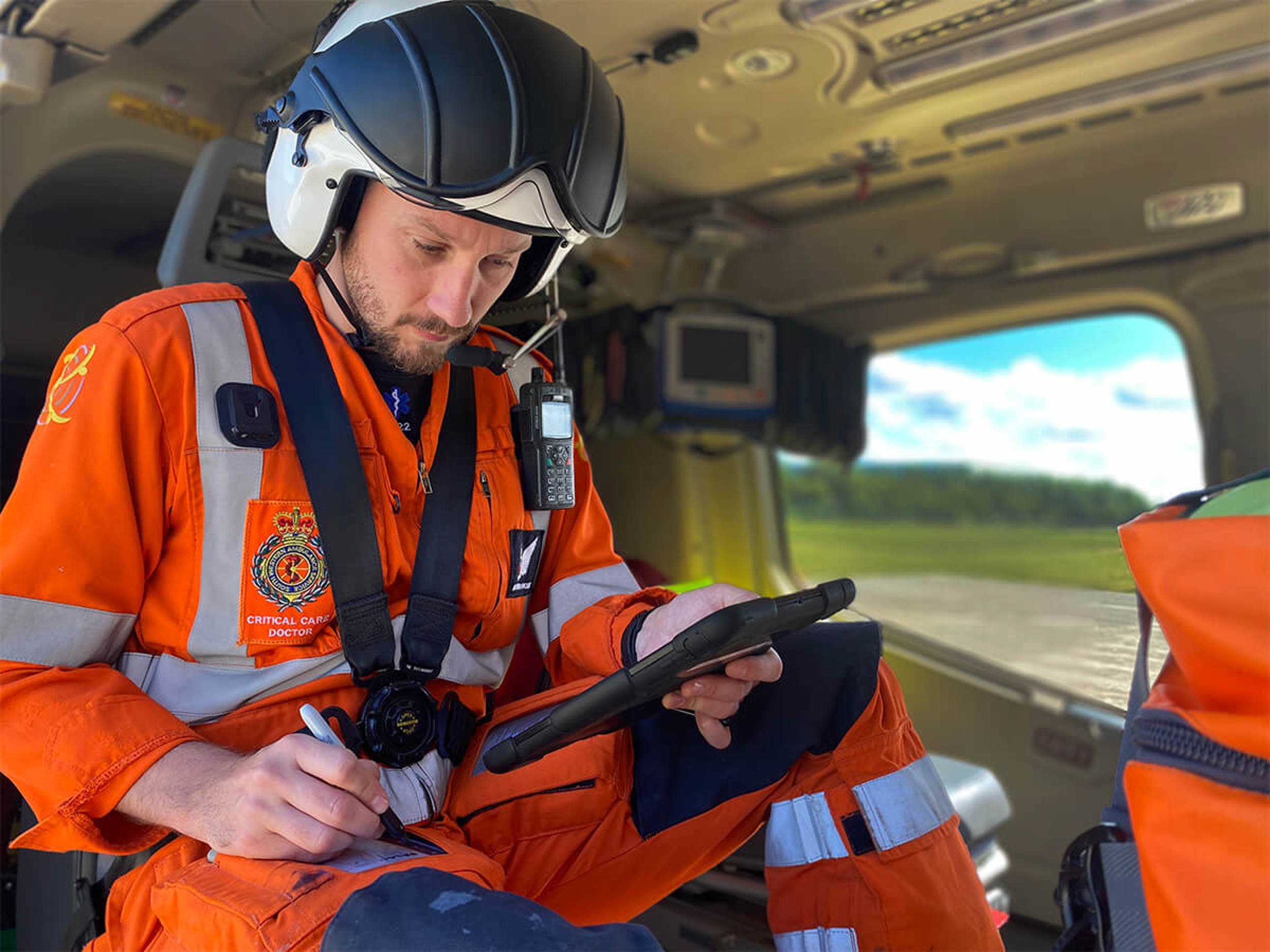 A doctor sat in the back of a helicopter holding an iPad and writing notes