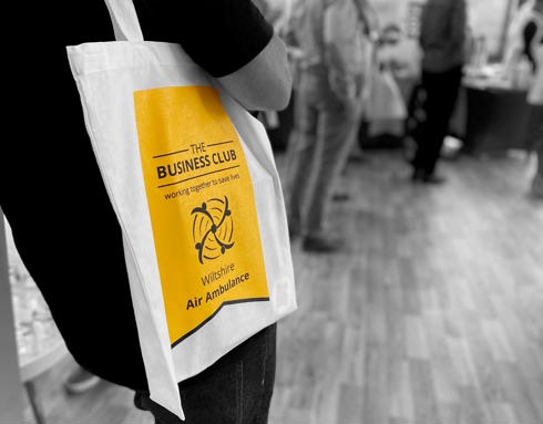 A person holding The Business Club branded tote bag