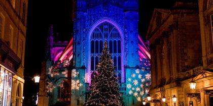 The exterior of Bath Abbey lit up with Christmas lights and a Christmas tree