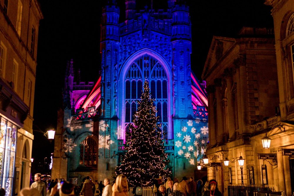The exterior of Bath Abbey lit up with Christmas lights and a Christmas tree