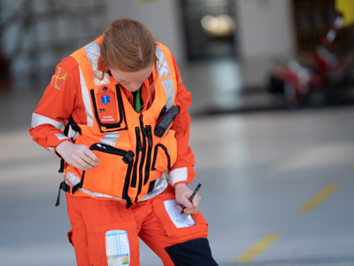 Paramedic Sophie Holt wearing orange flight suit and taking notes on leg pad