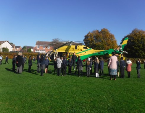 A yellow and green Wiltshire Air Ambulance helicopter surrounded by children