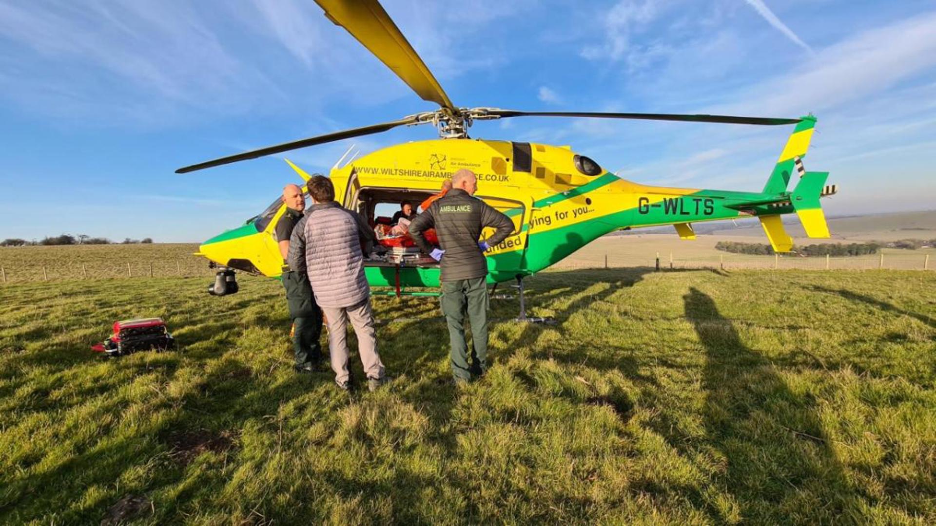 Wiltshire Air Ambulance's helicopter in a field, loading a patient on board