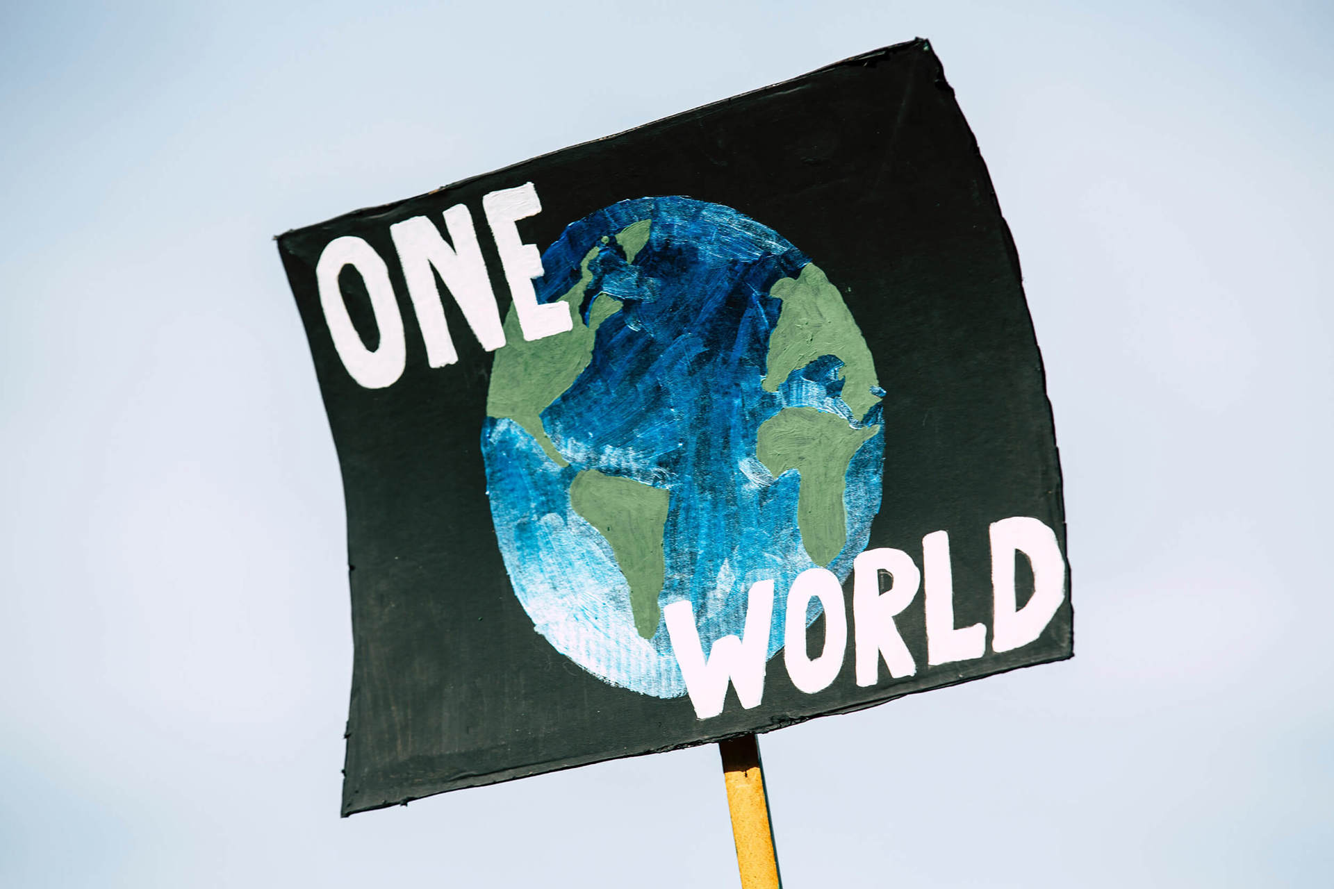A handmade sign showing a painting of the earth with 'One World' in white paint