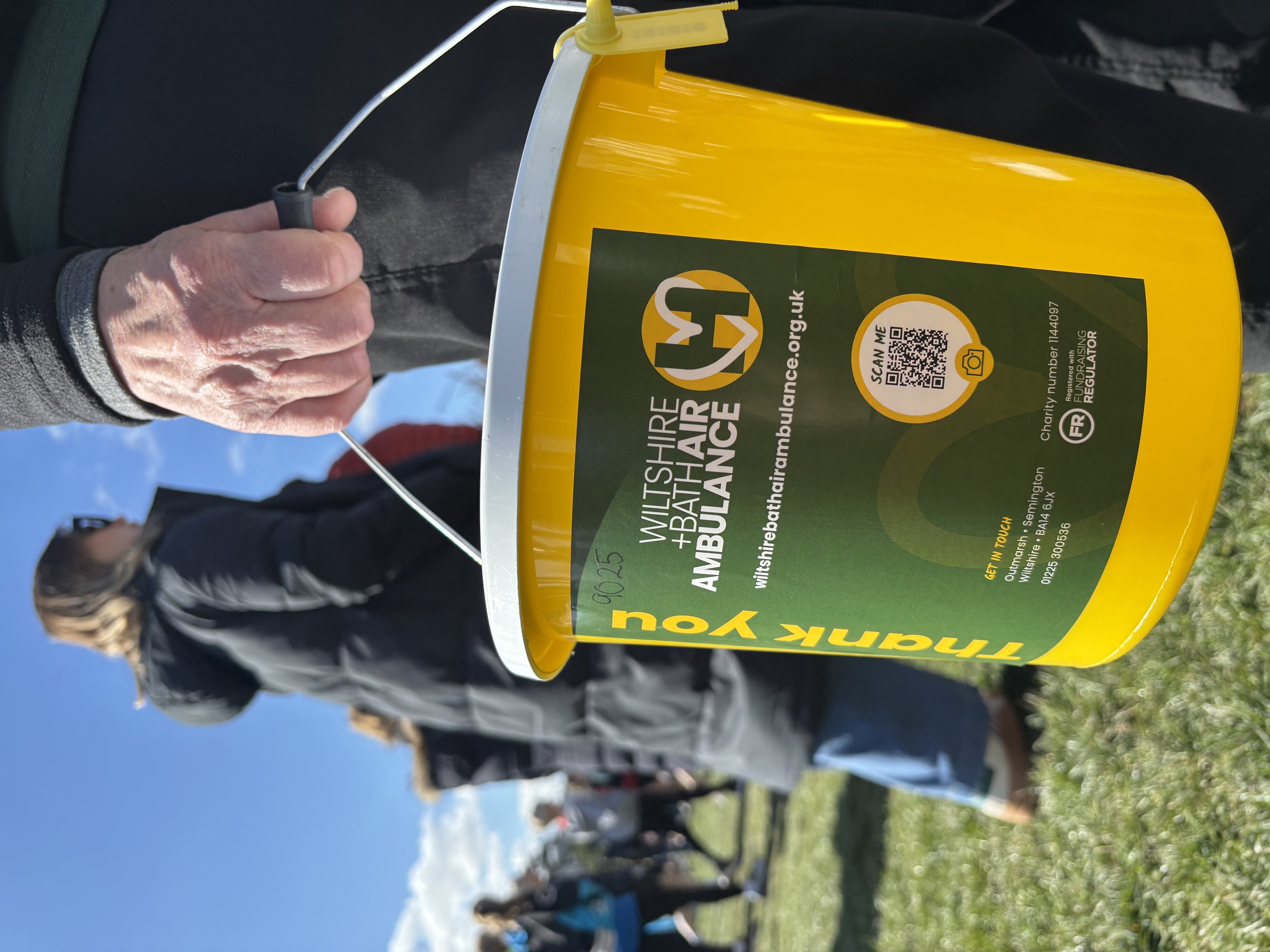 A yellow collection bucket with green label showing W+BAA logo and donation information