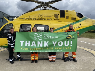 Wiltshire Air Ambulance paramedics and pilots holding a green thank you banner in front of the helicopter.