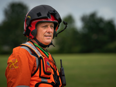 Paramedic Rich Miller wearing a red flight helmet and orange flight suit, with WAA avatar on the sleeve