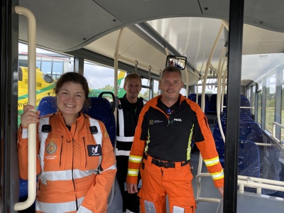 Paramedics Jo and Rocky, and Pilot Fin standing on a bus with the Wiltshire Air Ambulance helicopter in the background
