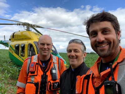 Paramedic Dan, pilot Elvis and paramedic Adam taking a selfie whilst standing in front of the Wiltshire Air Ambulance helicopter, which has landed in a field
